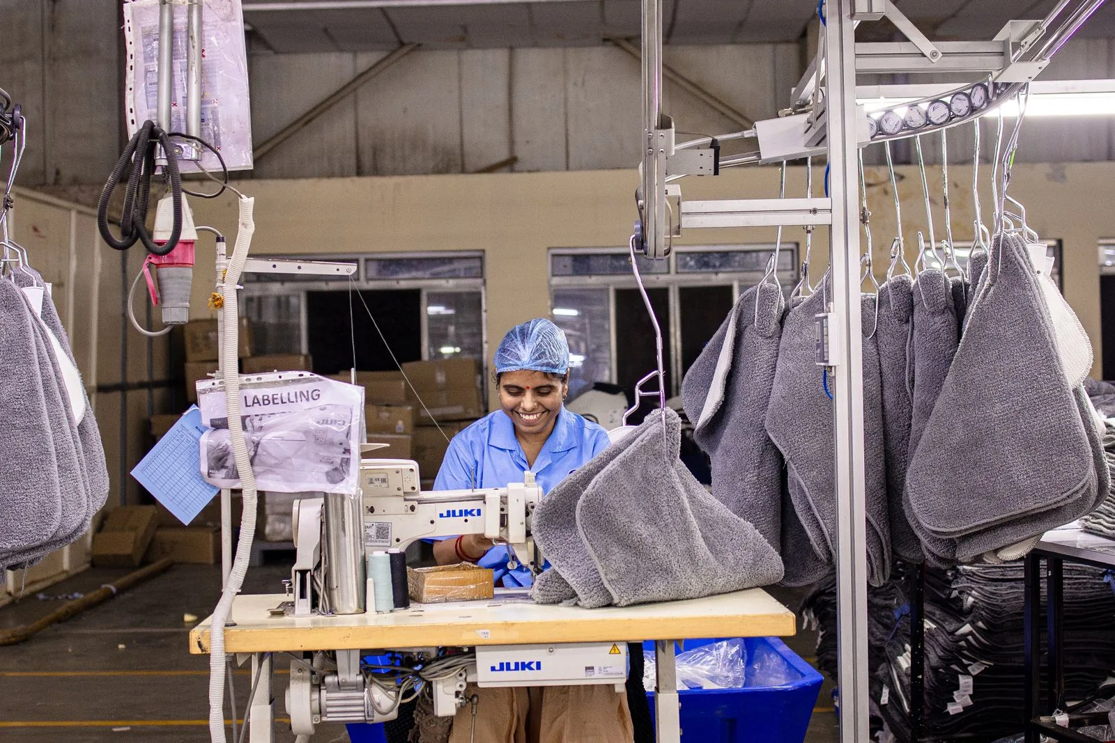 Operator at a Juki lockstitch machine on a garment sewing line, with bundles on an overhead hanger